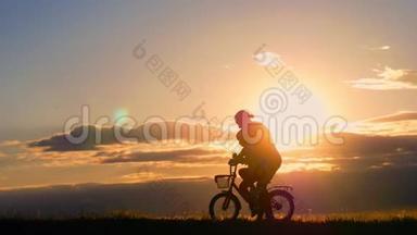 剪影自行车可爱的家庭在草地上日落时间。母亲和婴儿在日落时骑自行车的剪影。生活方式